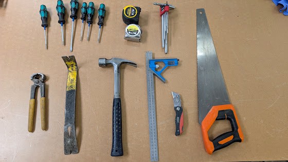 Carpenter's hand tool kit laid out: hand saw, hammer, combination square, tape measure and screwdrivers