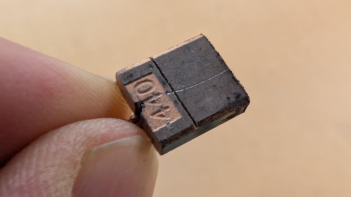 A worn carbon brush from a brushed power tool motor held between finger and thumb