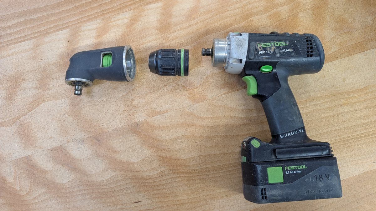 A Festool combi drill with its chuck removed, lying beside the chuck and a right-angle head